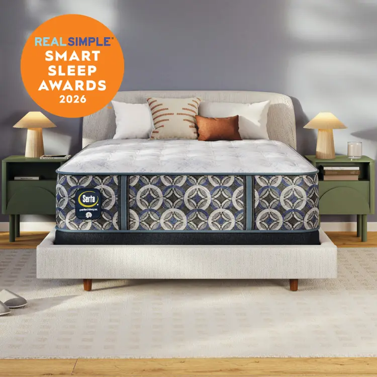 A Serta perfect sleeper plush mattress with a pattern matching upholstered base in a styled bedroom scene, with two green nightstands, lamps, pillows, and a gray wall. An orange circular badge in the upper left reads 'REAL SIMPLE SMART SLEEP AWARDS 2026.