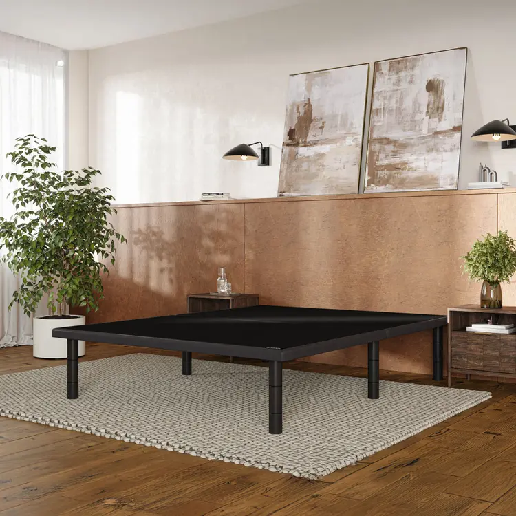 A black Baselogic Platform with four legs, set on a textured beige rug in a modern room with wood floors, a copper-colored accent wall, and abstract wall art.